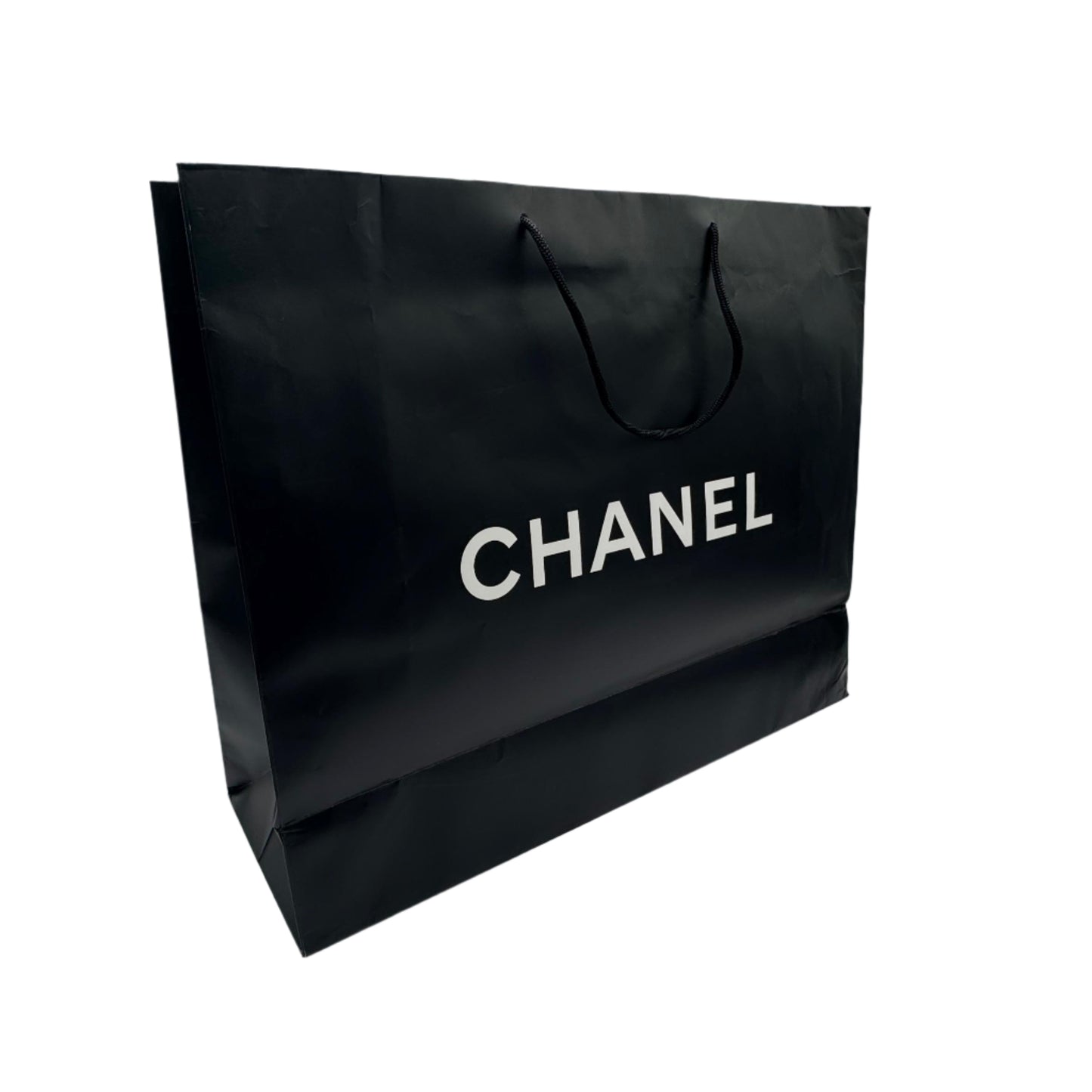 Black Chanel shopping bag on a white surface with a textured gray wall background
