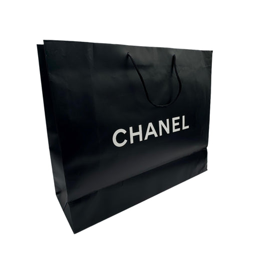 Black Chanel shopping bag on a white surface with a textured gray wall background
